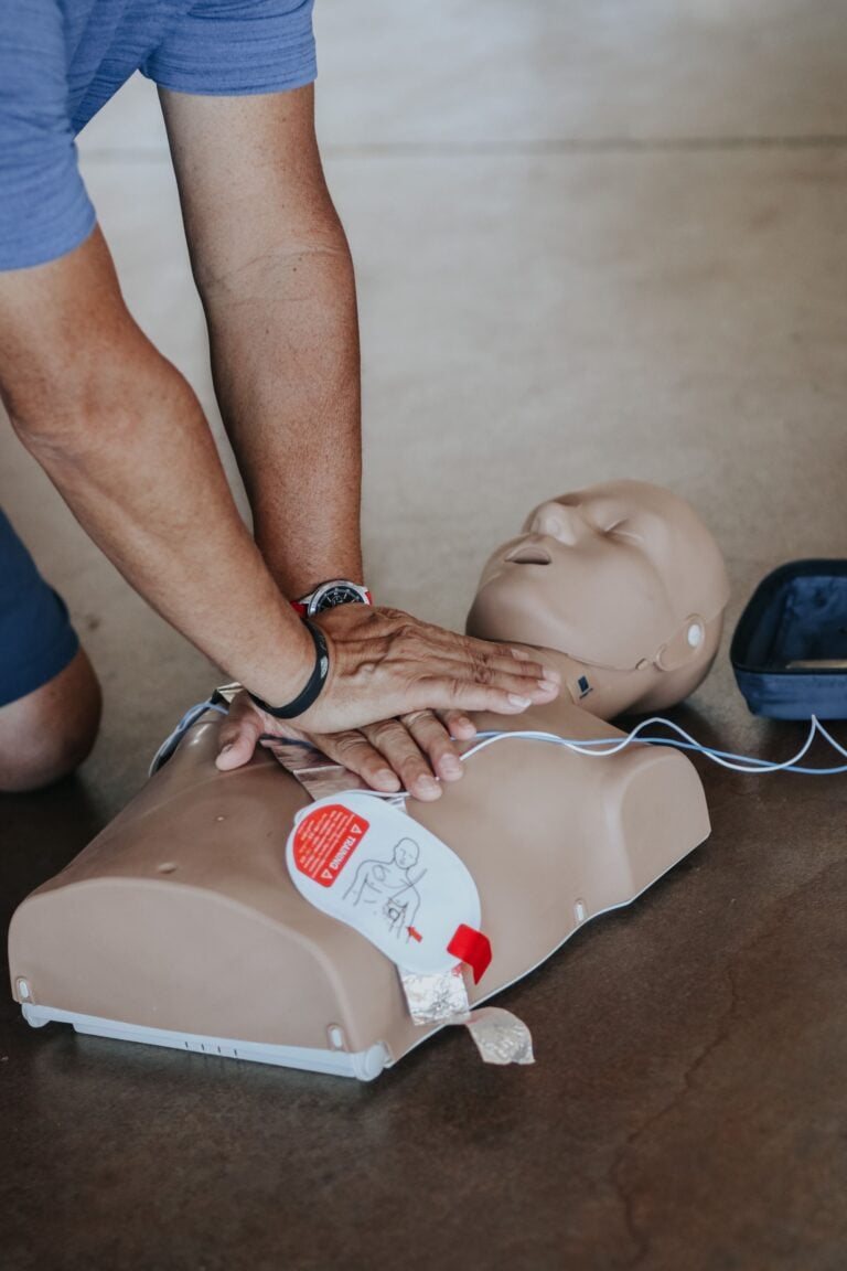 Hands performing chest compressions on a CPR manikin with AED pads attached